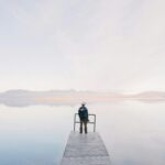 A solitary traveler stands on a dock enjoying the serene water view